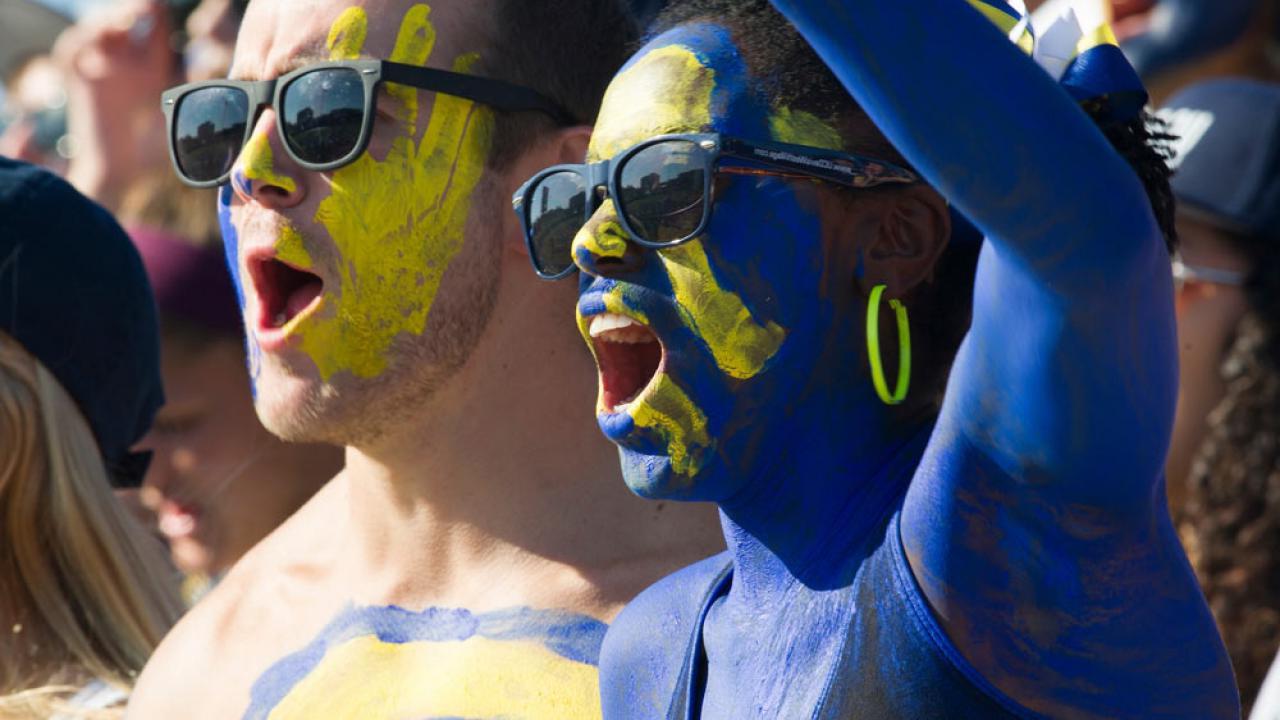 a male and female student painted in amjs澳金沙门 blue and gold cheer on the Aggies at the annual homecoming football game