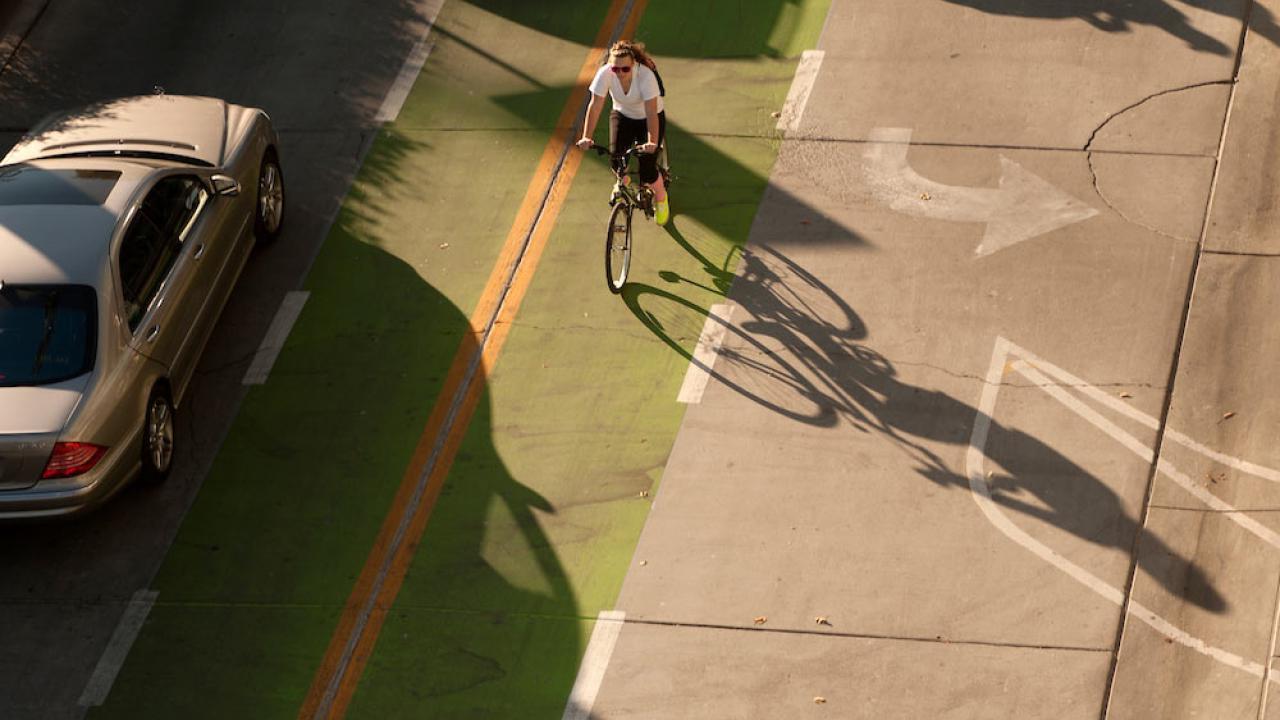 a female student rides her bike through a clearly marked green bike line next to a car on the UC Davis campus