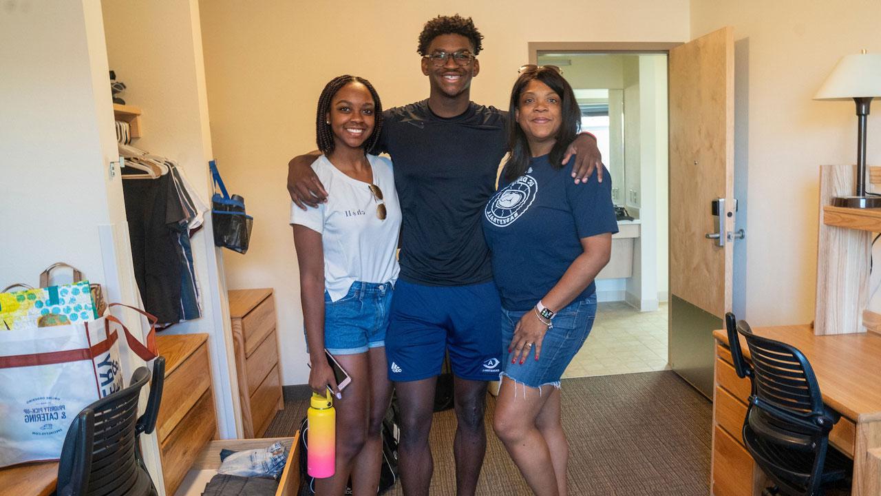 A new student smiles with his family as he moves into his residence hall.