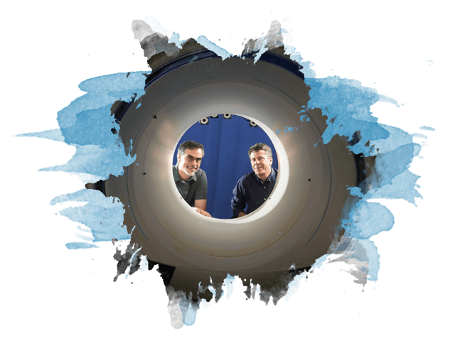 Two dudes look through the opening of a full body PET scanner