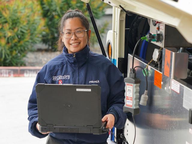 A woman holds a computer outside a bus's rear panel that is open