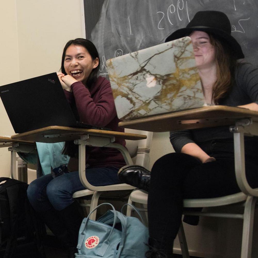 学生们坐在课桌前，对着笔记本电脑微笑