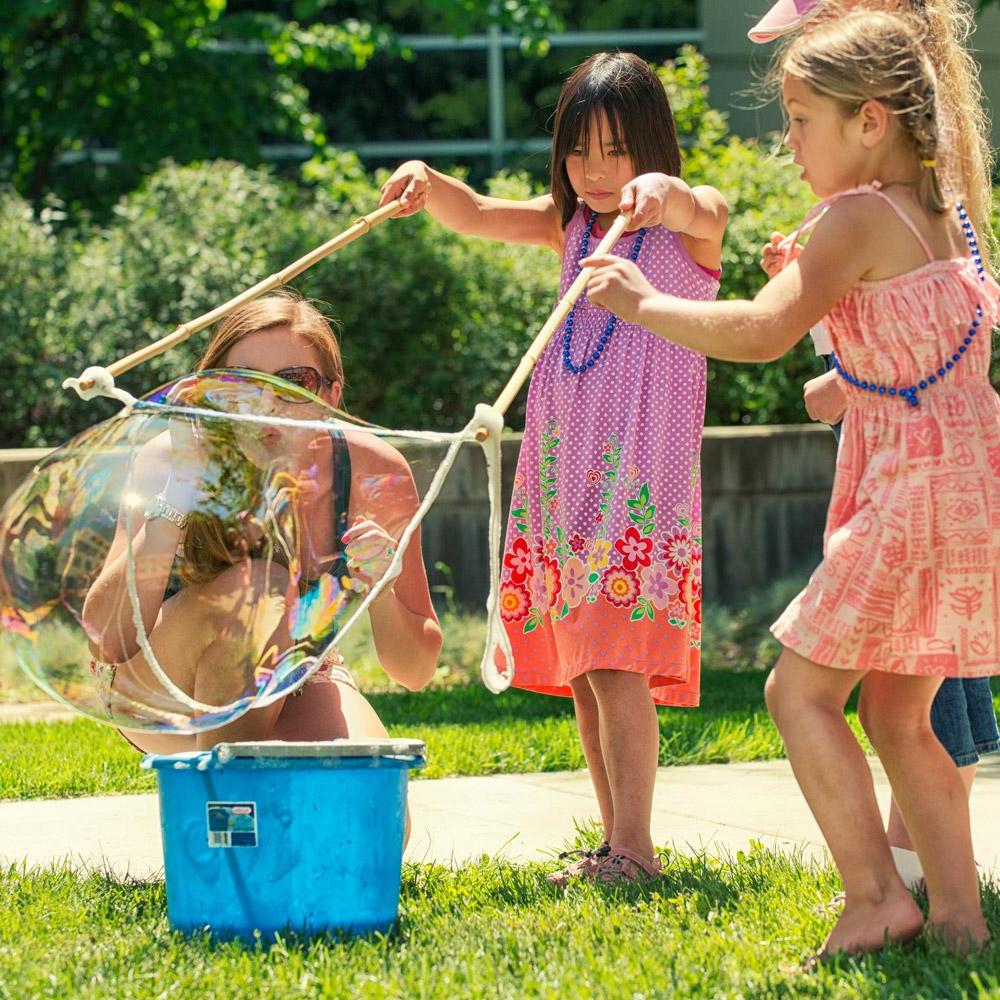 Two children and a parent blowing giant bubbles together