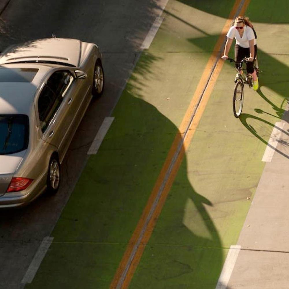 一名女学生在自行车道上骑自行车，旁边是一辆过往的汽车