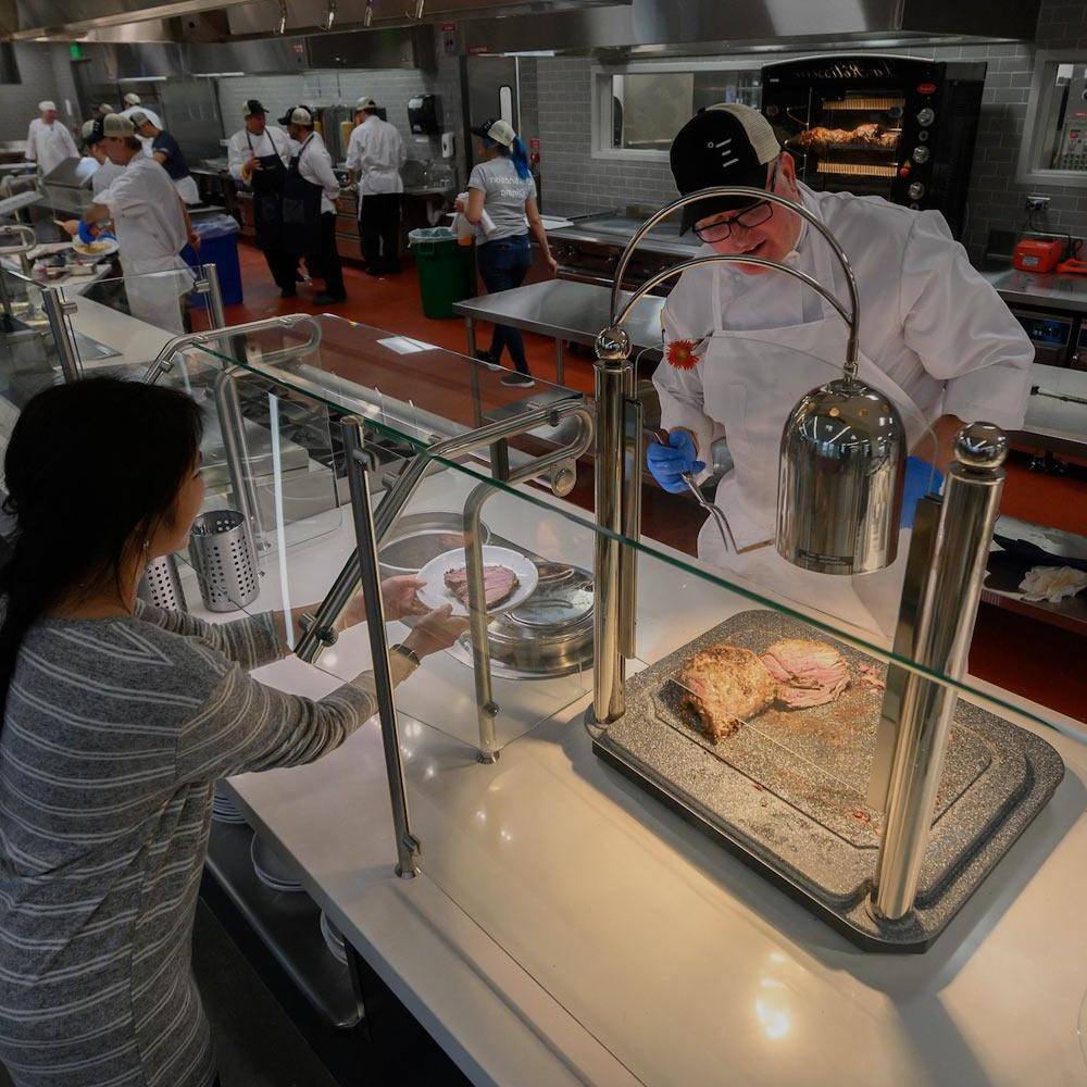 一名公共餐厅员工正在为amjs澳金沙门的一名学生端上一块肉