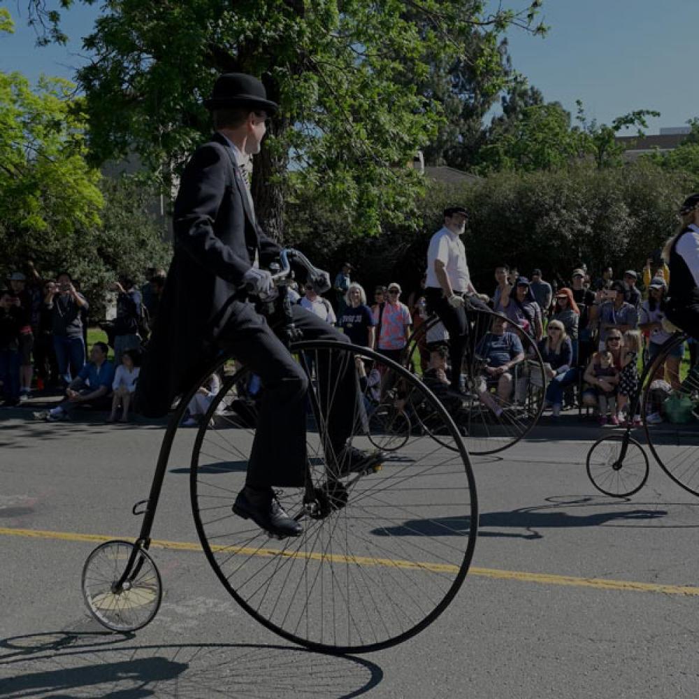 Two people riding penny farthing bicycles through Davis